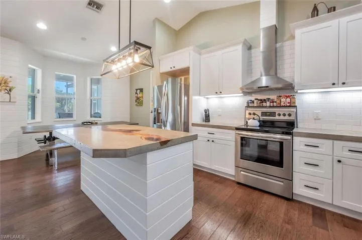 Kitchen with white cabinets, visible vents, wall chimney exhaust hood, dark wood finished floors, and appliances with stainless steel finishes
