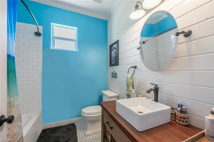 Bathroom with tile patterned flooring, shower / bathtub combination with curtain, vanity, crown molding, and toilet