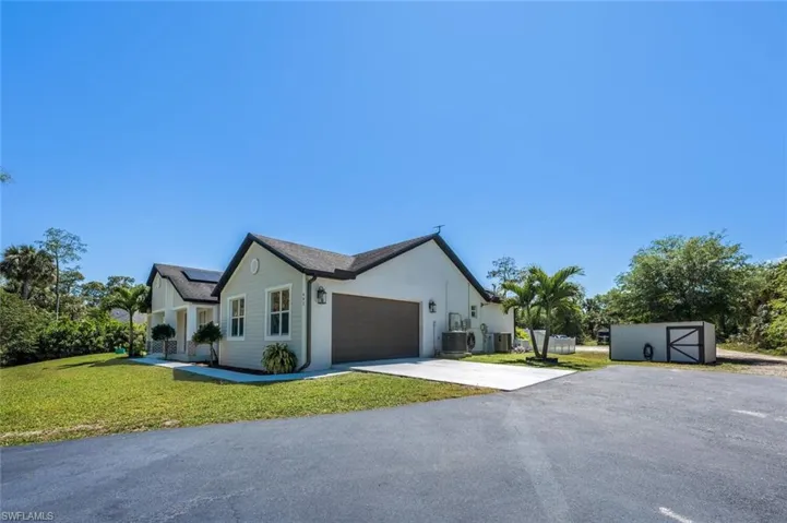 View of front of house with driveway, central AC unit, a front yard, solar panels, and a garage