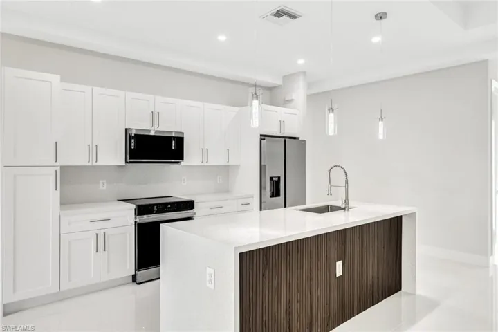 Kitchen featuring a kitchen island with sink, stainless steel appliances, decorative light fixtures, and sink