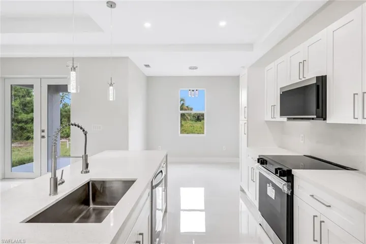 Kitchen featuring sink, white cabinetry, appliances with stainless steel finishes, decorative light fixtures, and light stone countertops