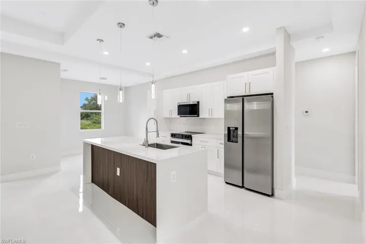 Kitchen with white cabinetry, an island with sink, pendant lighting, stainless steel appliances, and sink