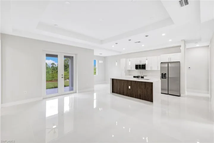 Kitchen with a raised ceiling, a center island with sink, stainless steel appliances, and white cabinets