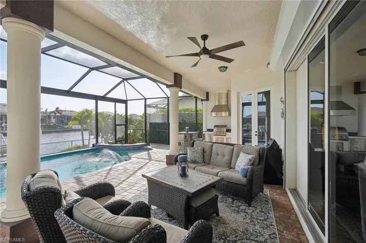 View of swimming pool featuring area for grilling, a patio area, glass enclosure, ceiling fan, and pool water feature