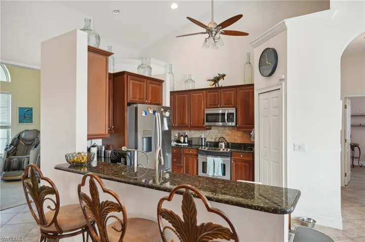 Kitchen featuring kitchen peninsula, dark stone counters, light tile patterned flooring, appliances with stainless steel finishes, and high vaulted ceiling
