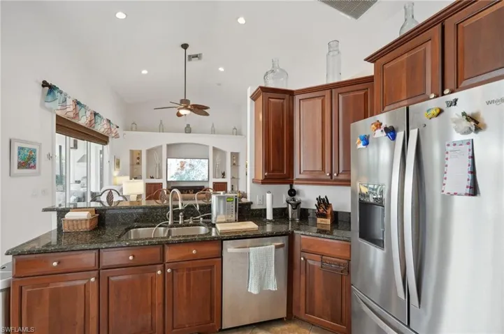 Kitchen featuring sink, ceiling fan, stainless steel appliances, dark stone counters, and high vaulted ceiling