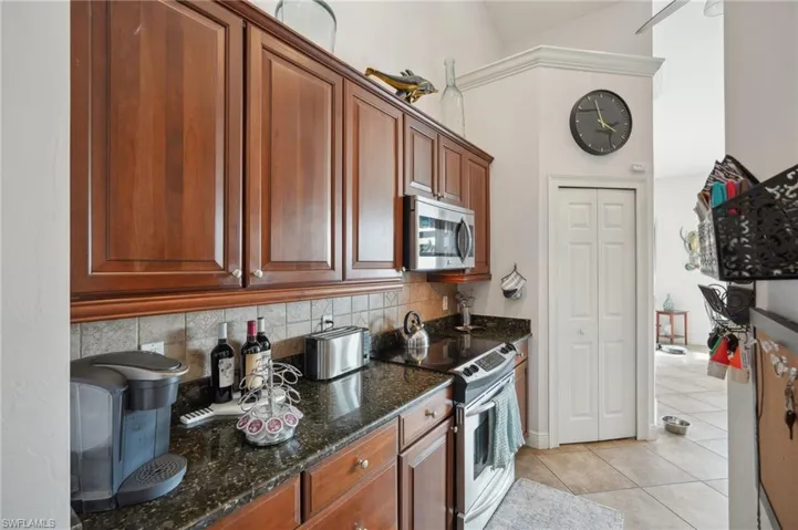 Kitchen with backsplash, dark stone counters, light tile patterned flooring, white electric stove, and high vaulted ceiling