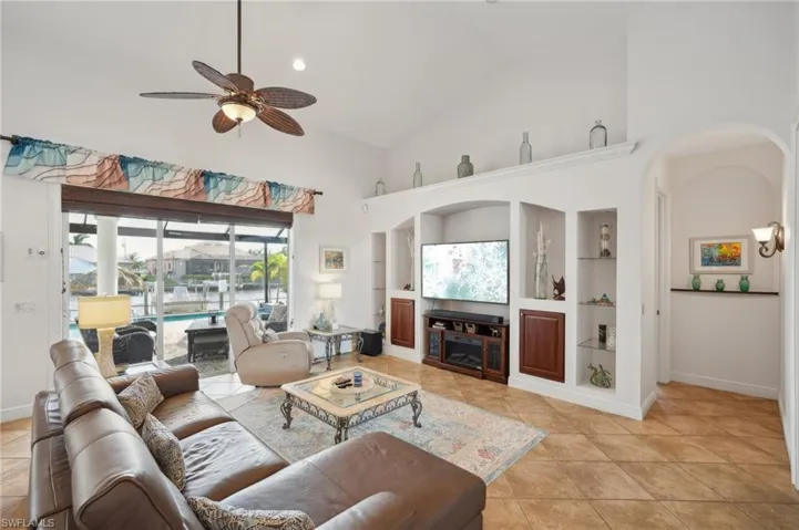 Living room featuring ceiling fan, high vaulted ceiling, light tile patterned flooring, and built in shelves