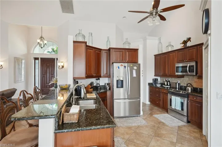 Kitchen with sink, kitchen peninsula, stainless steel appliances, dark stone countertops, and high vaulted ceiling