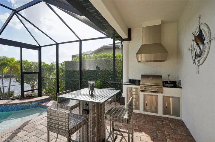 View of patio with exterior kitchen, glass enclosure, a fenced in pool, sink, and a grill
