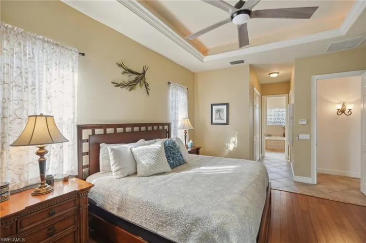 Bedroom featuring ceiling fan, hardwood / wood-style flooring, a tray ceiling, crown molding, and ensuite bath