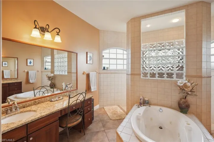 Bathroom featuring vanity, a relaxing tiled tub, tile walls, and tile patterned flooring