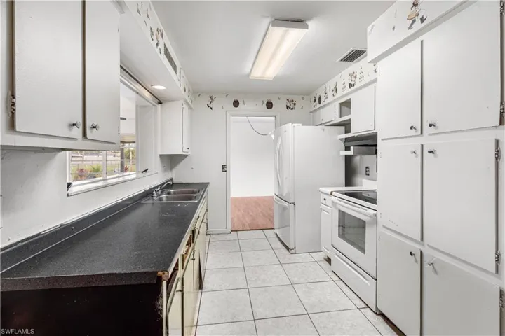 Kitchen featuring white appliances, sink, white cabinets, and light tile floors