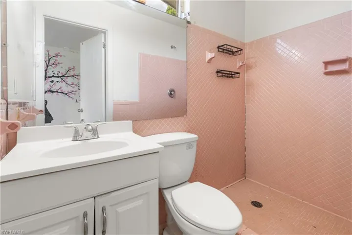 Bathroom featuring tiled shower, toilet, oversized vanity, and tile walls