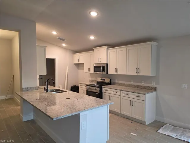 Kitchen featuring light-toned cabinetry, stainless steel appliances, granite countertops, and a central island with an undermount sink
