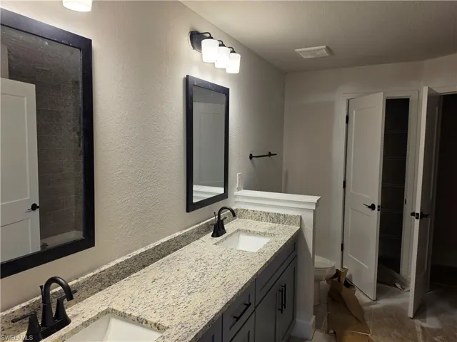 Dual vanity featuring granite-style countertops, matte black fixtures, and custom cabinetry