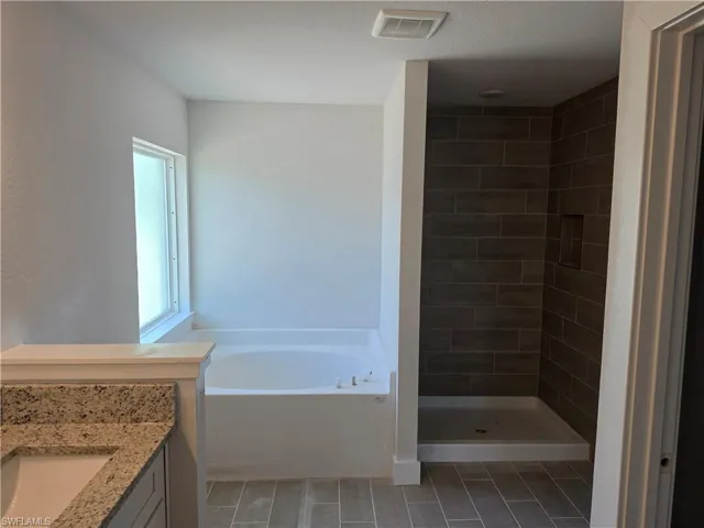 Bathroom featuring a built-in tub, a walk-in shower with tiled walls and a recessed niche, wood-finish tile flooring, a window, and a vanity with a granite countertop and an undermount sink