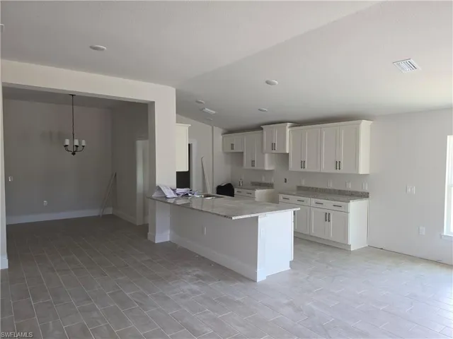Open-concept kitchen featuring an island with a granite countertop, white shaker-style cabinetry, and recessed lighting