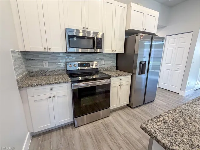 Kitchen featuring stainless steel appliances, dark stone counters, tasteful backsplash, white cabinets, and light wood finished floors