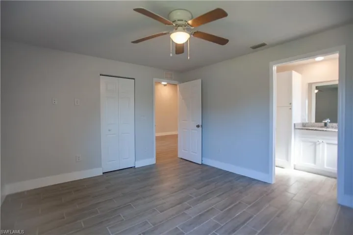 Unfurnished bedroom featuring a closet, wood finish floors, ceiling fan, and ensuite bathroom