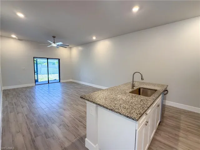 Kitchen featuring white cabinets, dark stone counters, an island with sink, light wood-type flooring, and a ceiling fan
