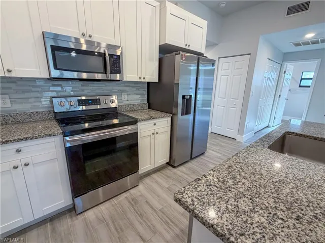 Kitchen featuring stainless steel appliances, light stone counters, decorative backsplash, white cabinetry, and light wood-type flooring