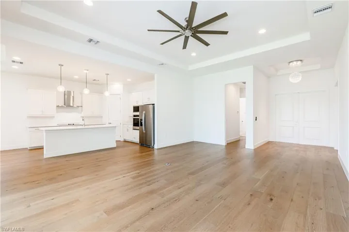 Unfurnished living room with light hardwood / wood-style floors, a raised ceiling, and ceiling fan