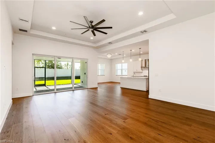 Unfurnished living room featuring ceiling fan, wood-type flooring, sink, and a tray ceiling