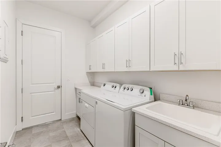 Laundry area featuring cabinets, separate washer and dryer, light tile patterned floors, and sink