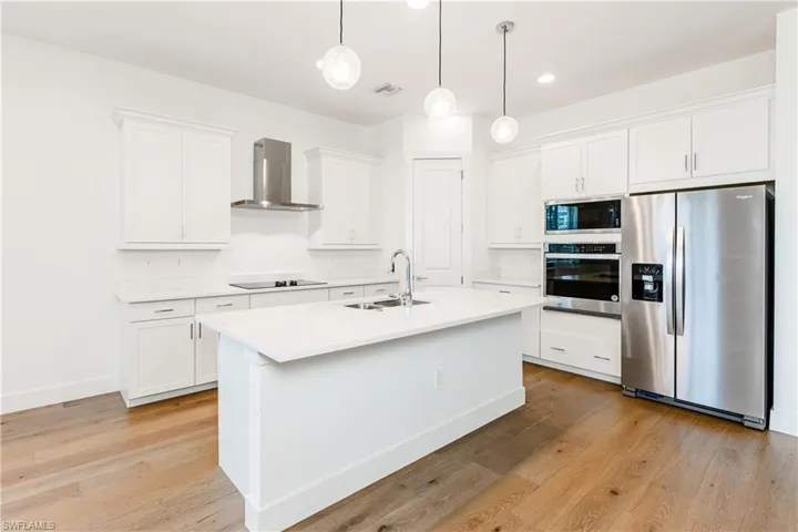 Kitchen featuring stainless steel appliances, an island with sink, light wood-type flooring, wall chimney exhaust hood, and sink