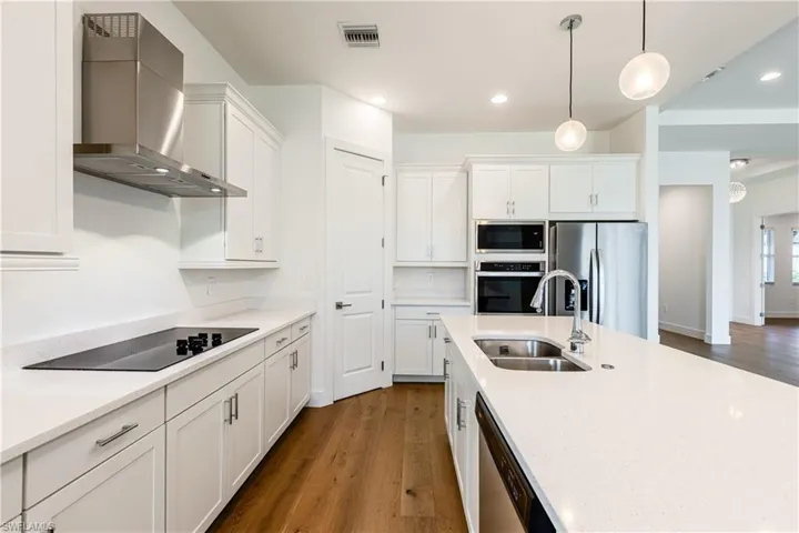 Kitchen with appliances with stainless steel finishes, white cabinets, wall chimney range hood, sink, and hardwood / wood-style flooring