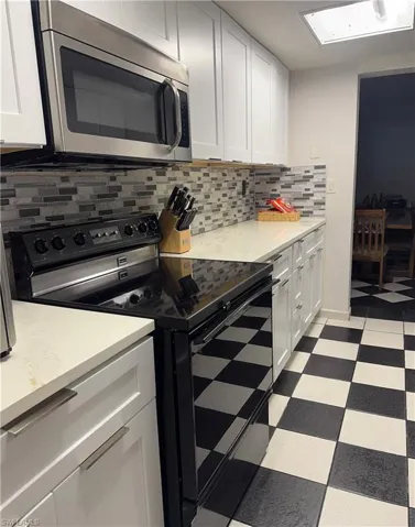 Kitchen featuring black / electric stove, stainless steel microwave, light floors, decorative backsplash, and white cabinetry