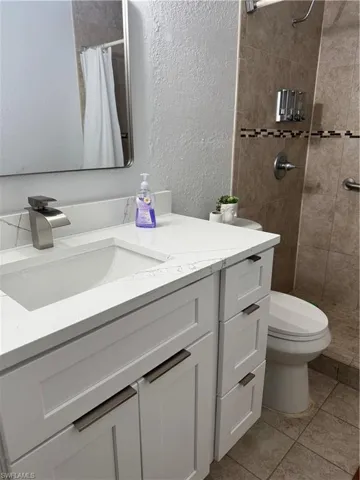 Full bath with vanity, a tile shower, a textured wall, and tile patterned flooring