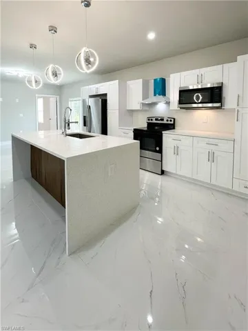 Kitchen with appliances with stainless steel finishes, white cabinets, and wall chimney exhaust hood