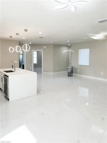Kitchen with a center island with sink, sink, hanging light fixtures, light tile patterned floors, and wine cooler