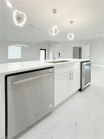 Kitchen with white cabinets, sink, pendant lighting, dishwasher, and beverage cooler