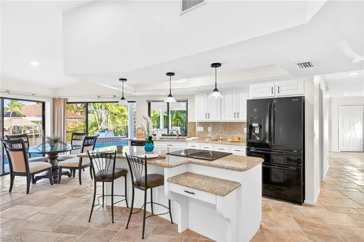 Kitchen featuring stone tile flooring, black appliances, light stone countertops, hanging light fixtures, and recessed lighting