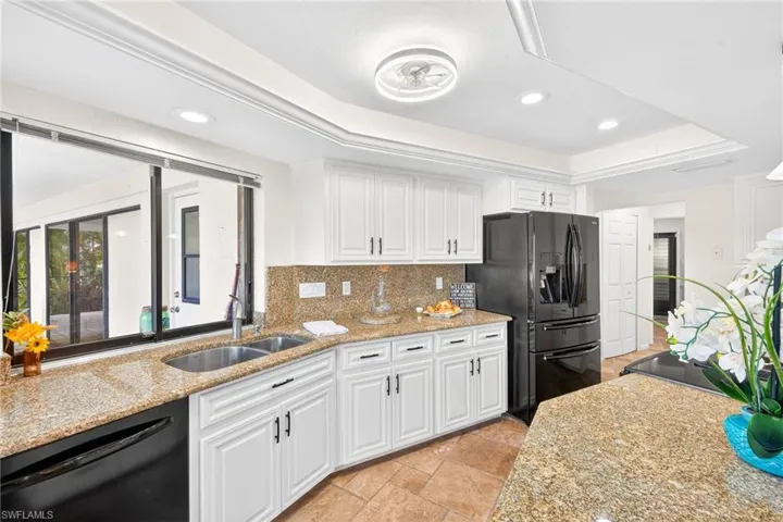 Kitchen featuring recessed lighting, white cabinetry, black appliances, light stone counters, and tasteful backsplash