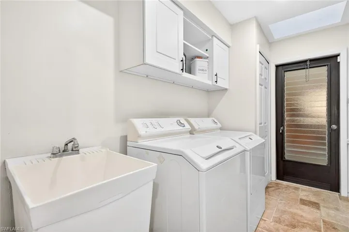 Washroom with stone tile flooring, a skylight, washing machine and clothes dryer, and cabinet space