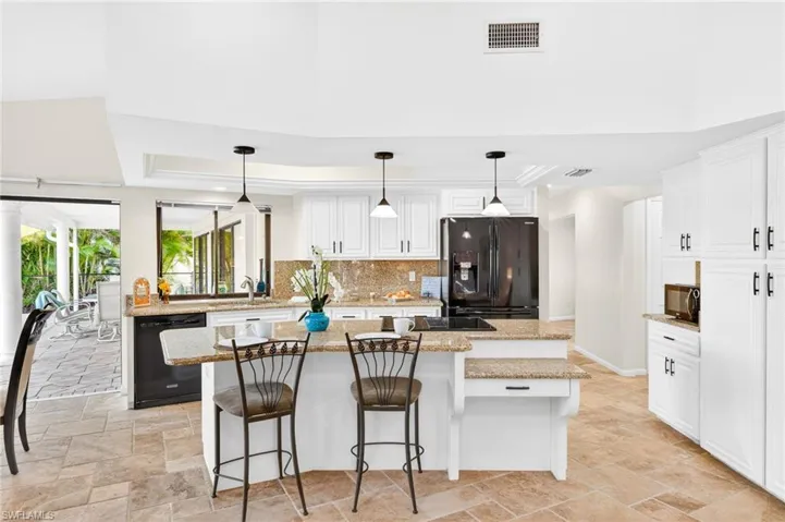 Kitchen with pendant lighting, a breakfast bar area, white cabinetry, black appliances, and light stone counters