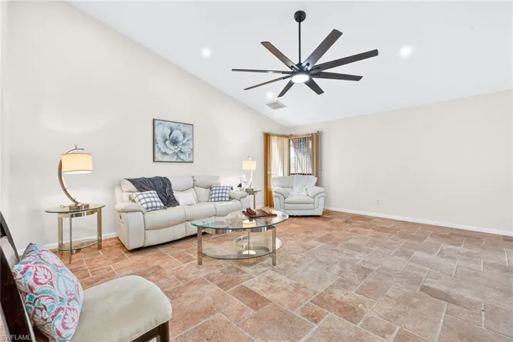 Living area with stone tile floors, high vaulted ceiling, recessed lighting, and a ceiling fan