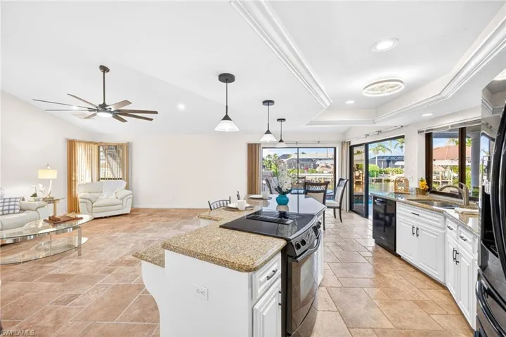 Kitchen featuring light stone countertops, black appliances, stone tile flooring, white cabinets, and recessed lighting