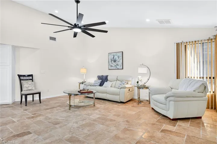 Living room featuring stone tile flooring, high vaulted ceiling, a ceiling fan, and recessed lighting
