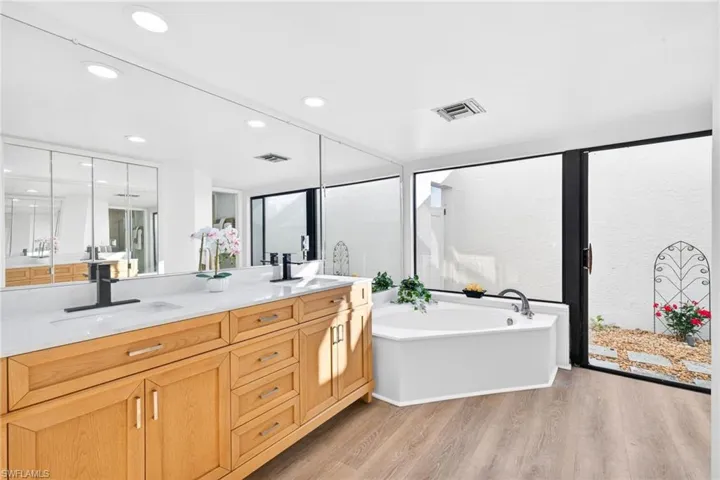 Bathroom featuring a bath, double vanity, light wood-type flooring, and recessed lighting with sliding door leading to a private spa like rock garden retreat
