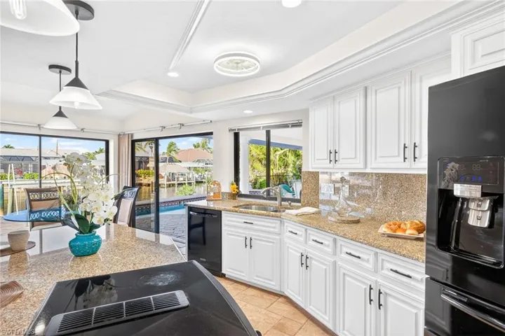 Kitchen featuring backsplash, black appliances, white cabinets, light stone countertops, and recessed lighting