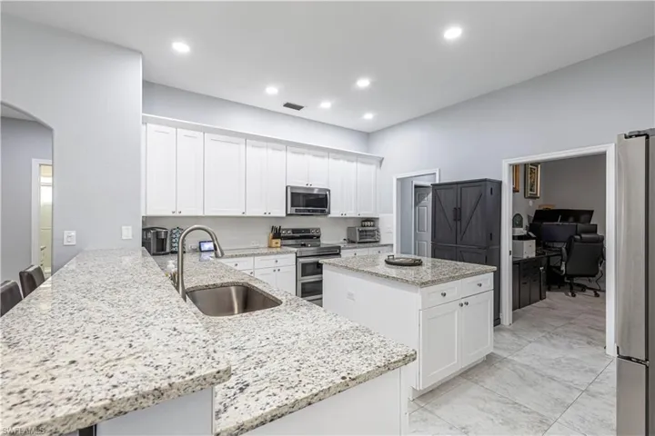 Kitchen with white cabinetry, a peninsula, stainless steel appliances, an office area, and arched walkways