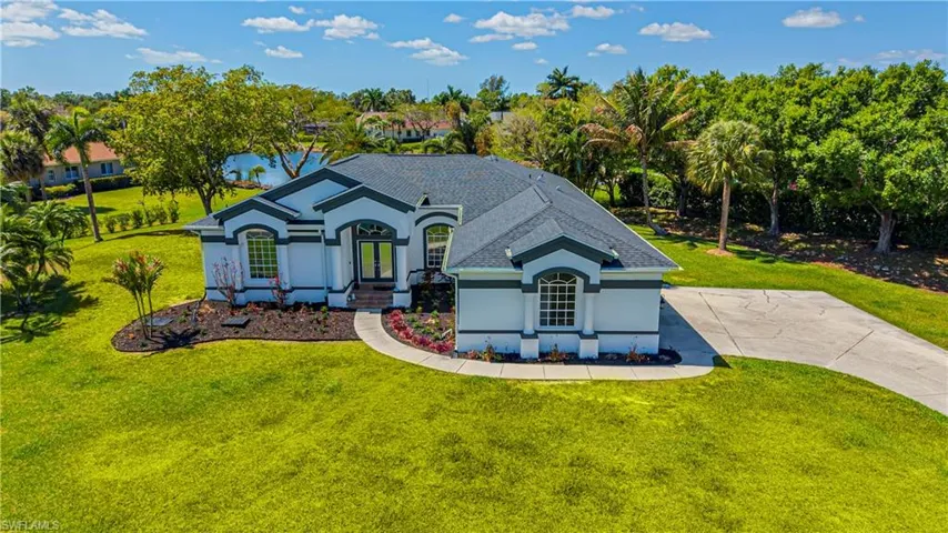 View of front of property featuring a front lawn, stucco siding, driveway, and view of wooded area