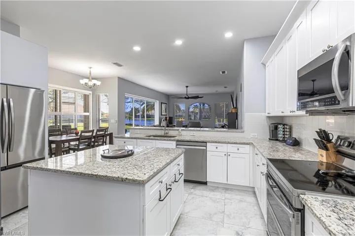 Kitchen with stainless steel appliances, a peninsula, light stone countertops, a center island, and white cabinetry