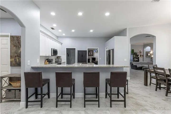 Kitchen featuring arched walkways, light stone countertops, a kitchen breakfast bar, a peninsula, and recessed lighting