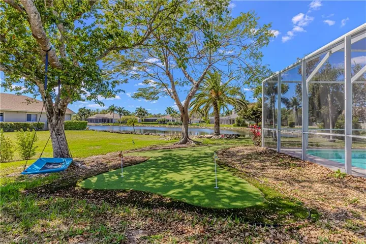 View of grassy yard featuring an area to practice putting, screen enclosure, outdoor pool & lake view